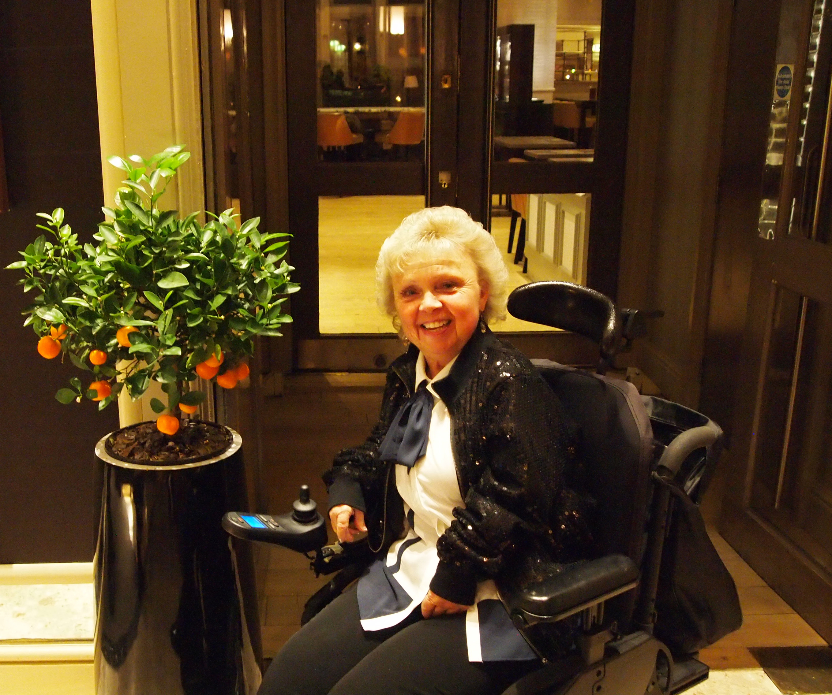 An image of Lynda. She is sitting in a wheelchair and smiling at the camera.