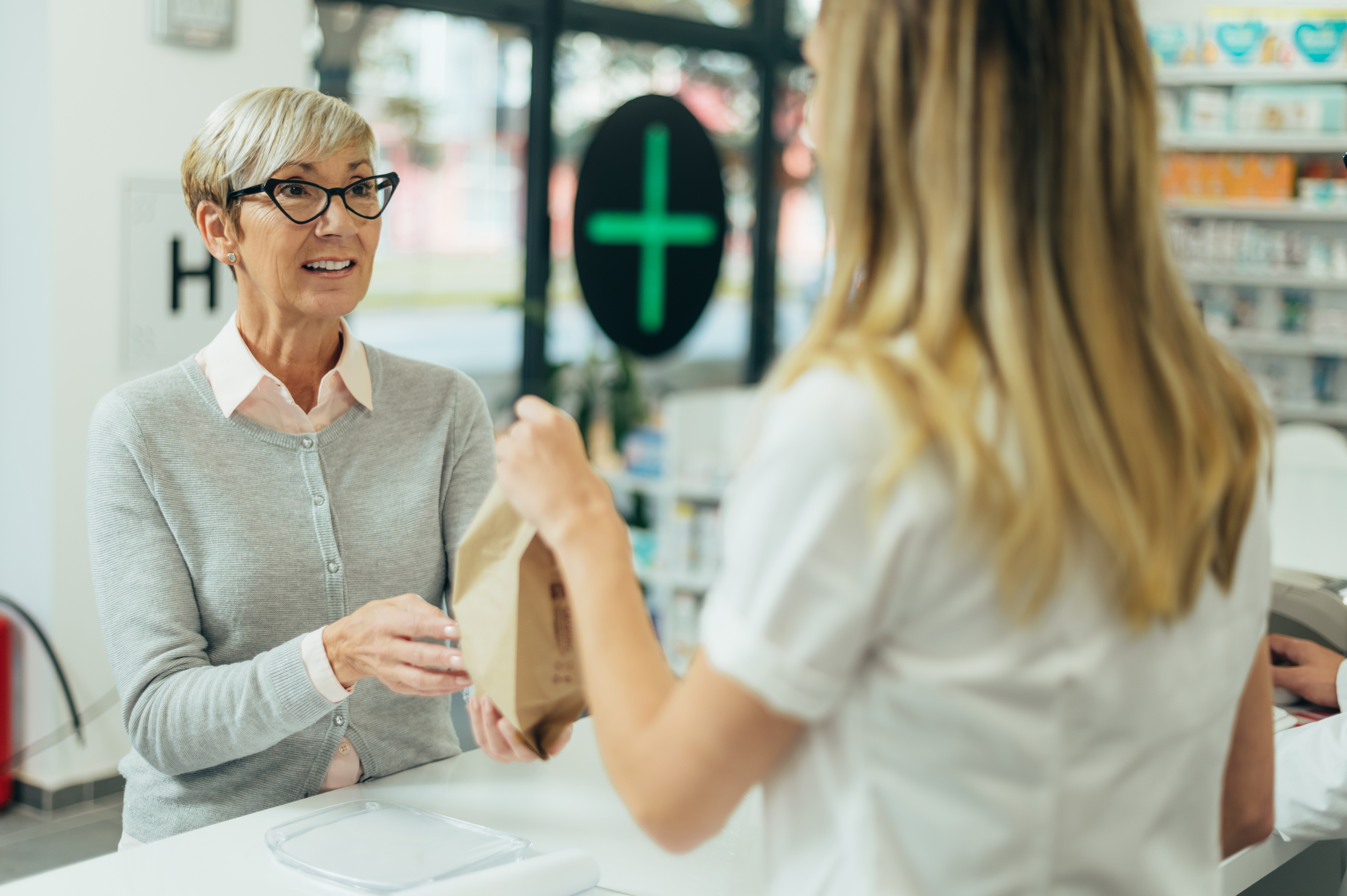 Senior woman customer buying medications at drugstore while talking with a female pharmacist