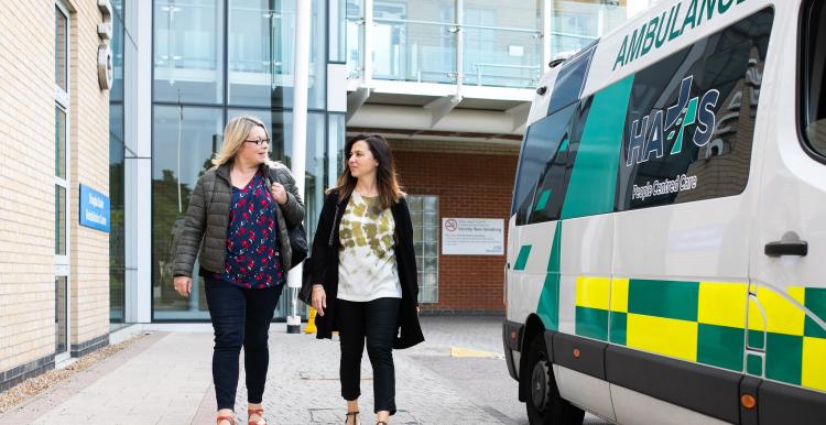 Two women outside a hospital near an ambulance