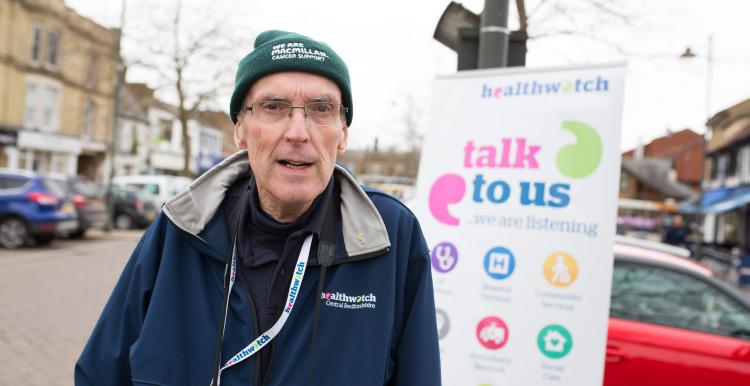 Male volunteer standing in front of a banner "Talk to us" 