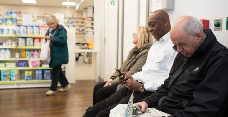 Three people sat waiting in a pharmacy