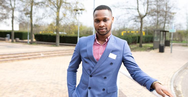 man wearing a suit standing in an open park leaning on a fence