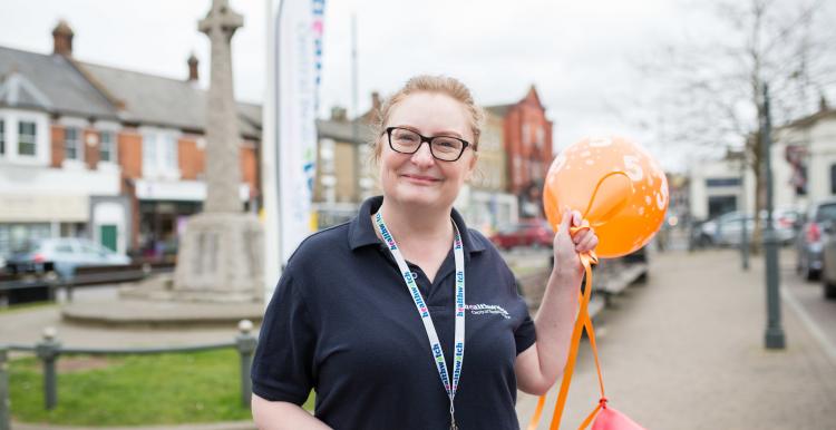 Woman holding balloons in front of a Healthwatch banner