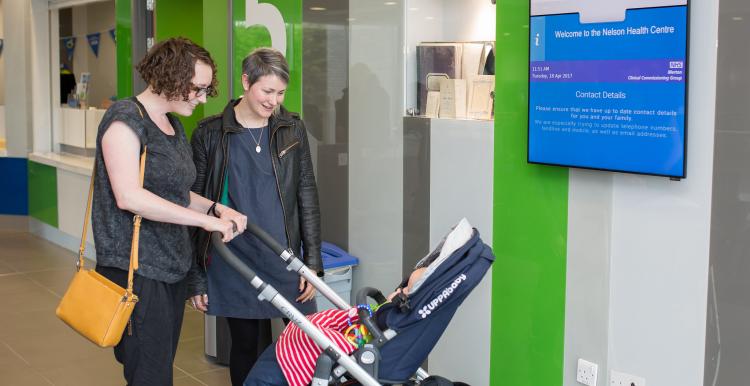 Two women smiling down at a baby in a pushchair