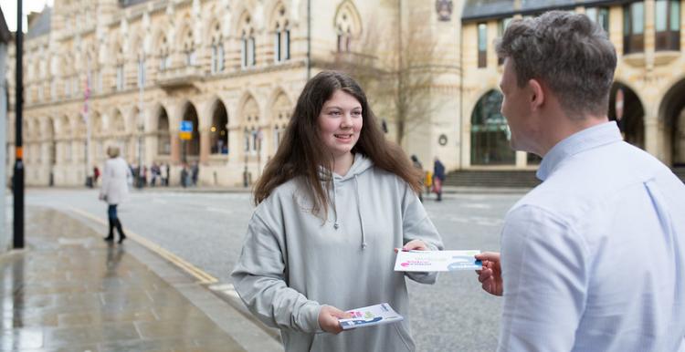 Teenage girl giving a leaflet to someone