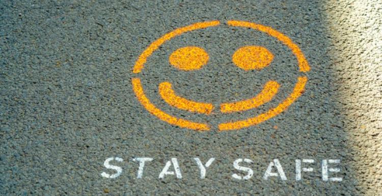 A yellow smiling emoticon and white texts saying 'stay safe' spray painted onto the road. 