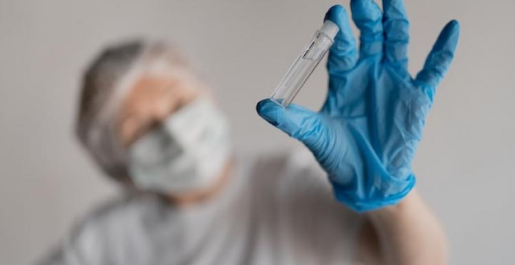 a hand in a medical glove holds an ampoule close-up, against the background of a blurred face in a mask