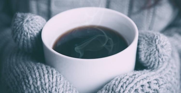 Gloved hands hold a hot cup of coffee