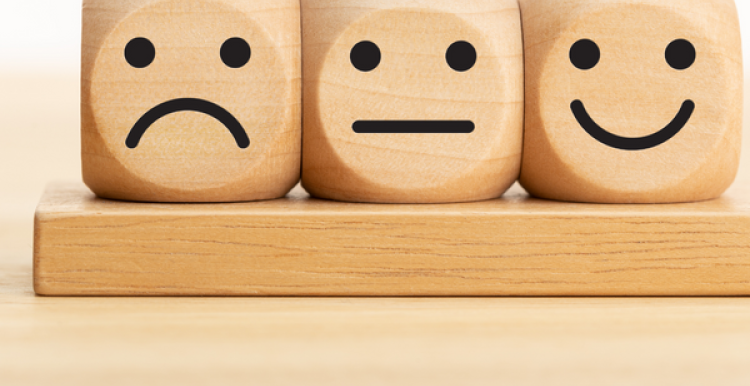 Three wooden dice showing a sad, neutral, and happy face