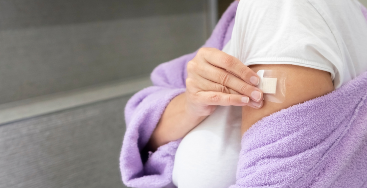 A woman in a purple bath robe places a HRT patch on her arm