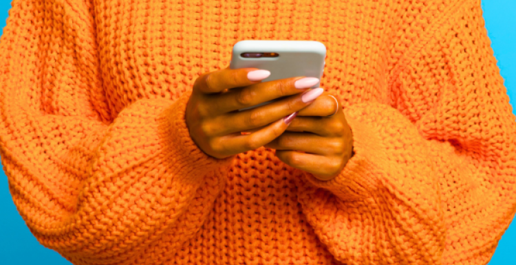 A photograph of a person in a bright orange jumper holding a phone. Only their torso is visible.