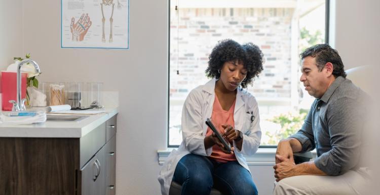 The mid adult female doctor points out something on the digital tablet as the mature adult male patient listens carefully.