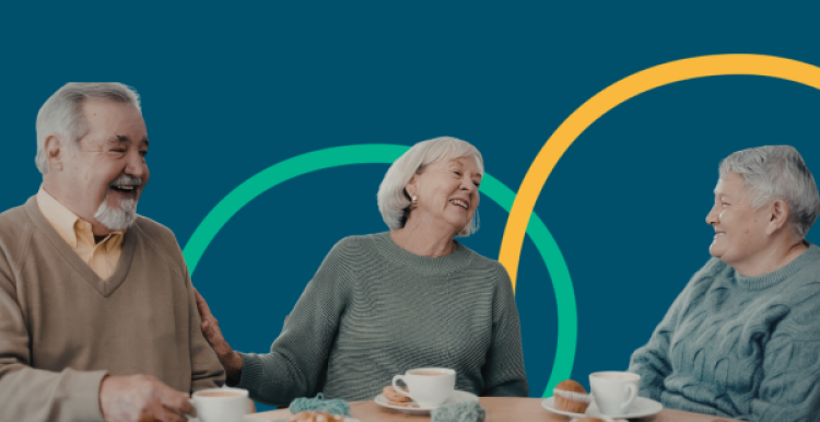 three older adults laughing together over cups of tea at a table