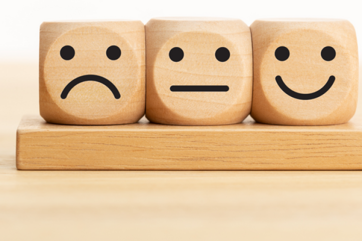 Three wooden dice showing a sad, neutral, and happy face