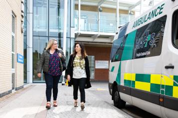 Two women outside a hospital near an ambulance