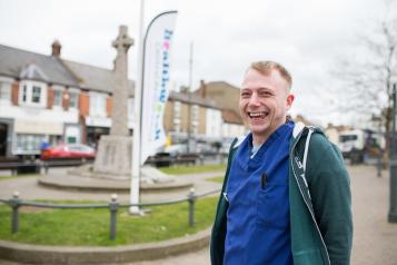 Man in scrubs in front of a Healthwatch banner