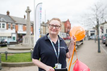 Woman holding balloons in front of a Healthwatch banner