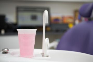 Dentist office showing a sink and plastic cup of mouthwash