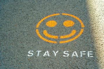 A yellow smiling emoticon and white texts saying 'stay safe' spray painted onto the road. 