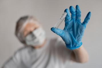 a hand in a medical glove holds an ampoule close-up, against the background of a blurred face in a mask