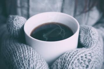 Gloved hands hold a hot cup of coffee