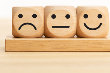Three wooden dice showing a sad, neutral, and happy face