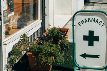 A pharmacy swingboard with a green cross and an arrow pointing to a shop