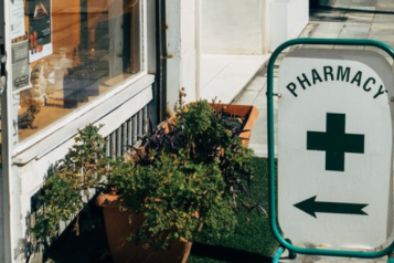 A pharmacy swingboard with a green cross and an arrow pointing to a shop 