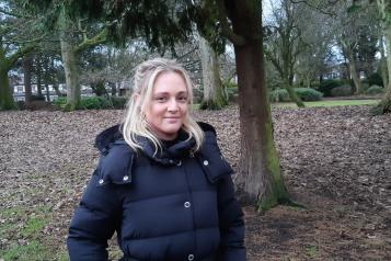 Ashley, a young white woman with blonde hair, standing in a wood