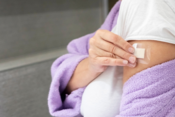 A woman in a purple bath robe places a HRT patch on her arm