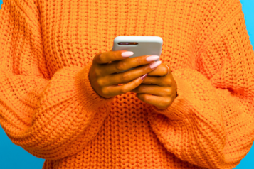 A photograph of a person in a bright orange jumper holding a phone. Only their torso is visible.