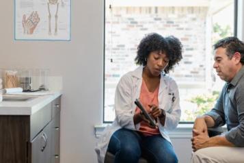 The mid adult female doctor points out something on the digital tablet as the mature adult male patient listens carefully.