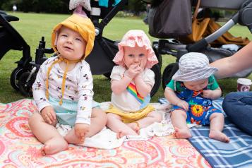 Three babies at a picnic in the park sitting on a blanket