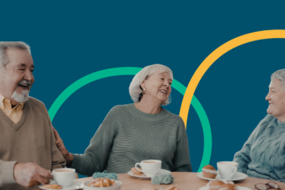 three older adults laughing together over cups of tea at a table