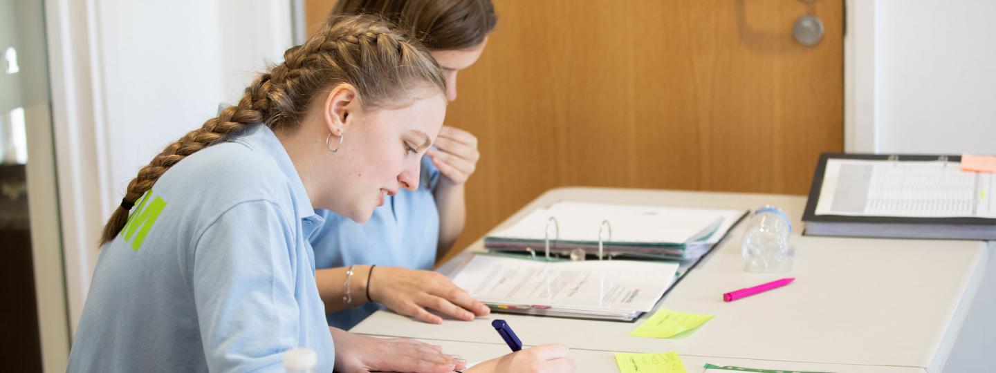 Two young girls sitting at a desk filling in forms